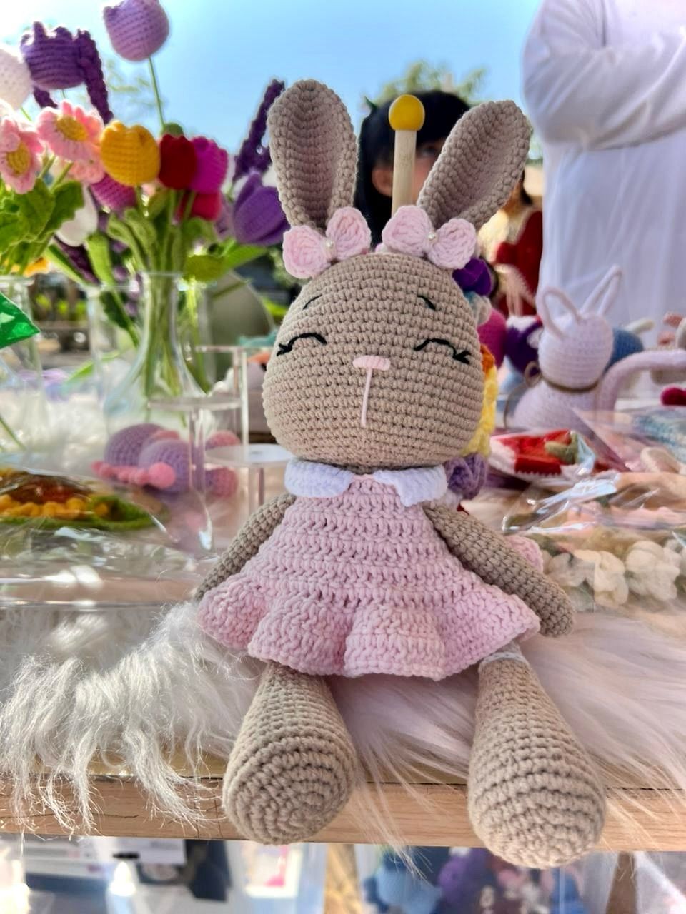 A pink-dressed crochet bunny amigurumi seated among fresh flowers.