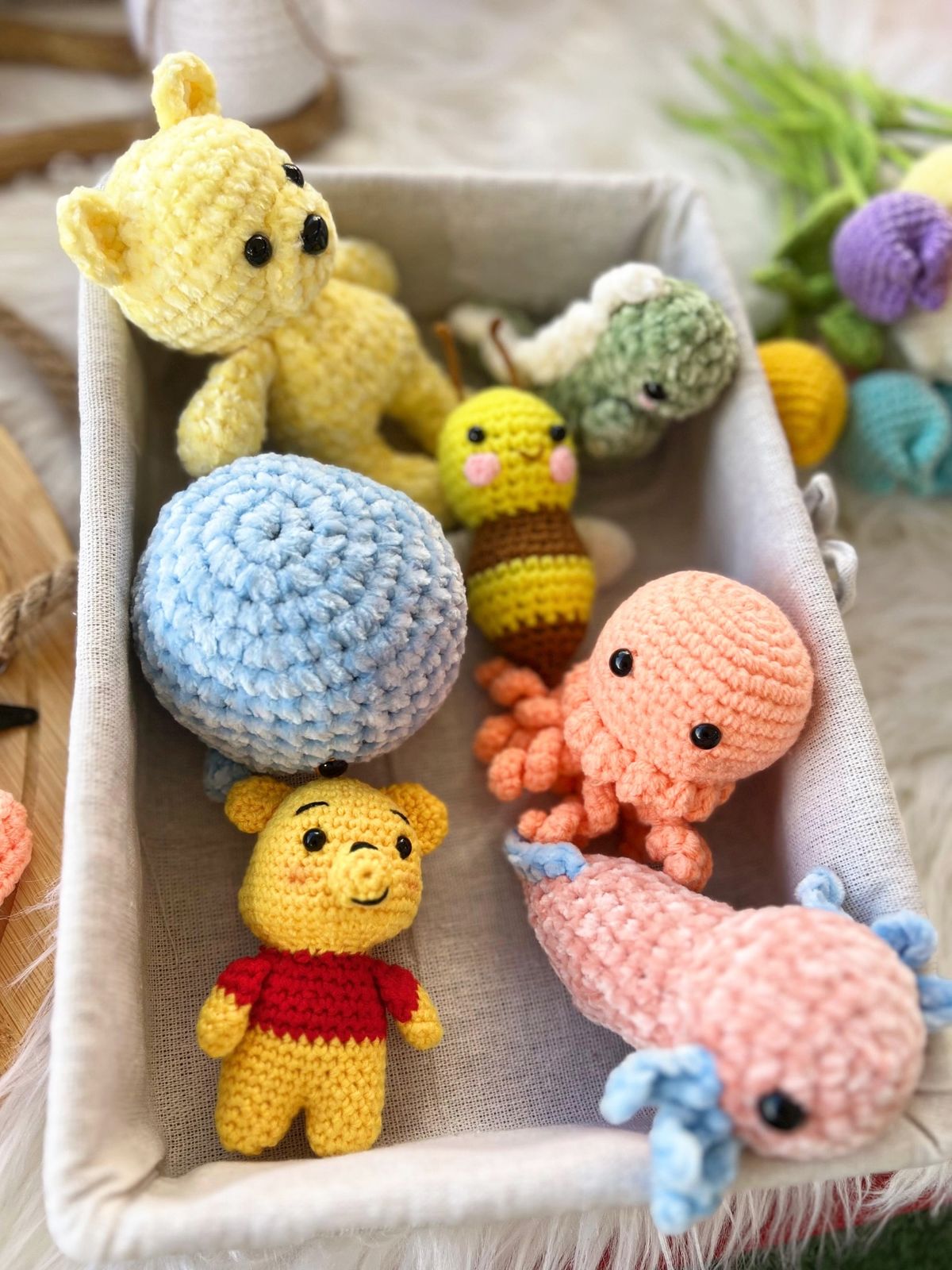 A basket of colorful amigurumi crochet toys, including a yellow bear, Winnie the Pooh, a bee, an octopus and a snail.