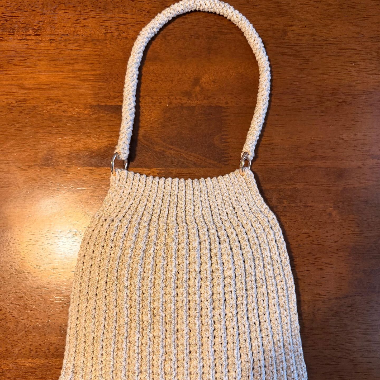 A cream crochet handbag with a woven handle, resting on a wooden table.